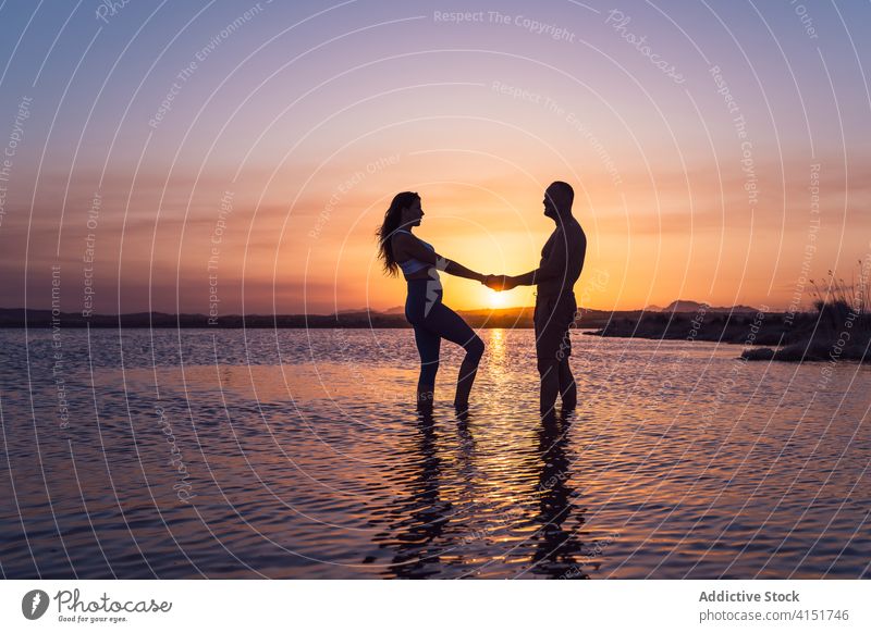 Unerkanntes Paar bei Sonnenuntergang am See stehend Wasser aktiv Partnerschaft Händchenhalten romantisch Liebe Silhouette Natur Dämmerung Abenddämmerung Sommer