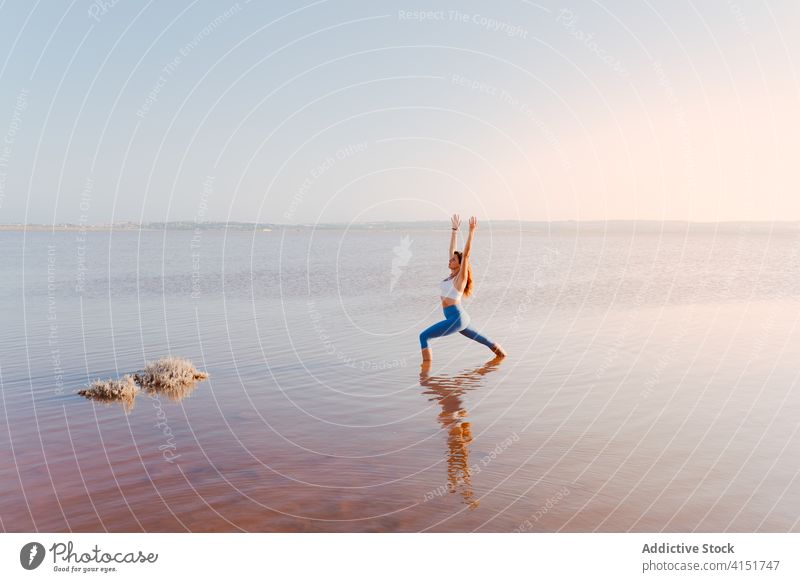 Frau übt Yoga-Asana im Wasser eines Sees üben Pose stehen Warrior One virabhadrasana Abend Gleichgewicht Windstille Fokus Harmonie Wellness Wegbiegung