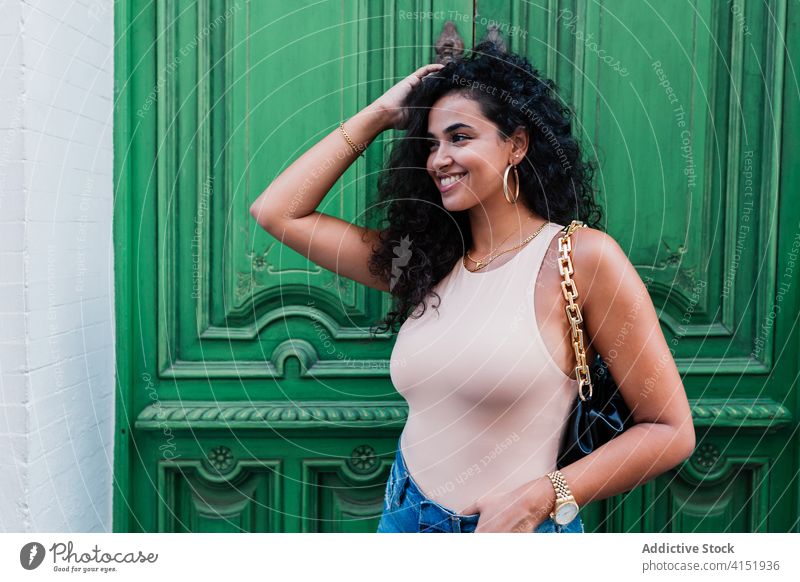 Glückliche ethnische Frau, die in der Nähe einer alten Tür steht jung krause Haare Stil brünett trendy heiter urban Freude Lächeln lässig Latein Lifestyle