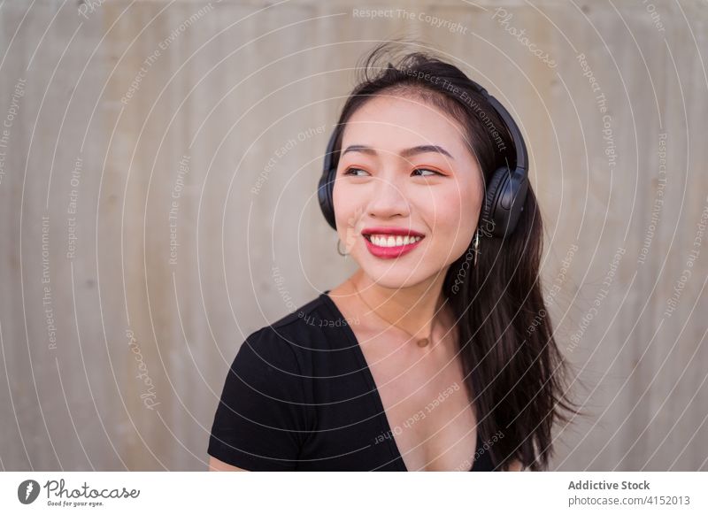Unbekümmerte Frau, die mit Kopfhörern Musik hört zuhören sorgenfrei Smartphone benutzend genießen ethnisch asiatisch Glück heiter Freude Klang modern Apparatur