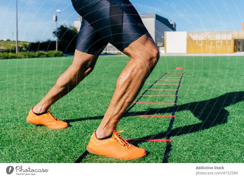 Athletischer Sportler beim Training auf einer Schnelligkeitsleiter im Stadion Laufmasche Beweglichkeit Geschwindigkeit Gerät Übung Mann muskulös Fitness