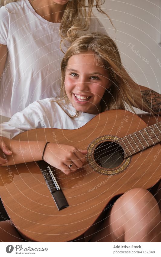 Porträt eines blonden Mädchens, das Gitarre spielt und in die Kamera lächelt, mit einer Frau, die neben ihm sitzt vertikal Musik Lehrer Bildung Lernen Schüler