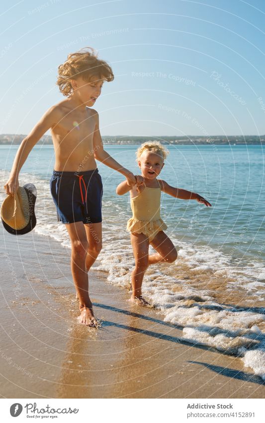 Vertikales Foto von zwei Kindern in Badeanzügen, die sich beim Spielen am Meer an den Händen halten primär Schwester Vertrauen anhänglich Teilen Gefühl Moment
