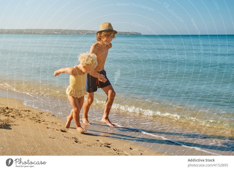 Zwei Kinder in Badeanzügen, die sich an den Händen halten, laufen gemeinsam am Meer entlang primär Schwester Vertrauen anhänglich Teilen Gefühl Moment Bruder