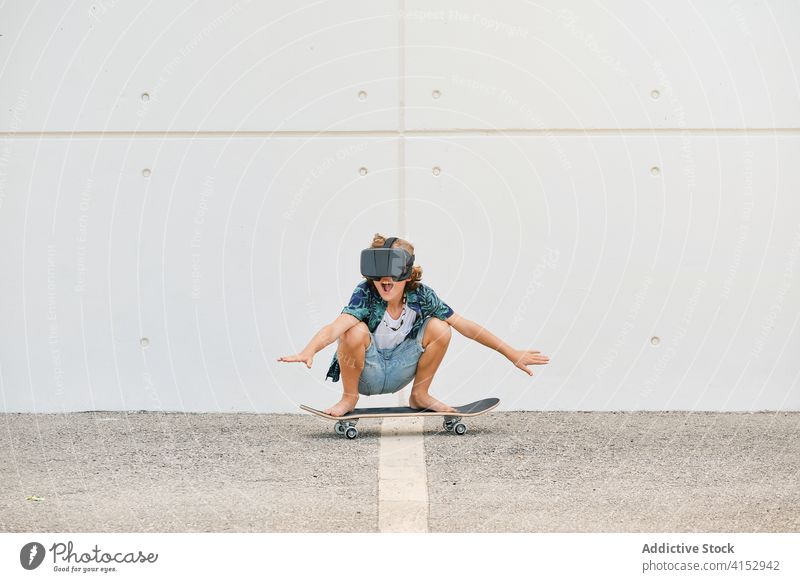 Junge in Sommerkleidung, der mit einer Virtual-Reality-Brille auf einem Skateboard fährt Reaktionen u. Effekte berührend gestikulierend optisch dimensional