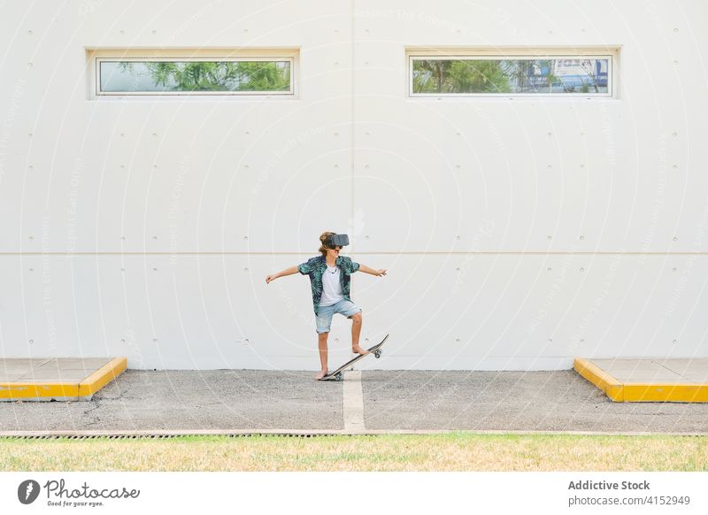 Kind macht einen Trick auf dem Skateboard mit Virtual-Reality-Brille auf einem Parkplatz Reaktionen u. Effekte berührend gestikulierend optisch dimensional