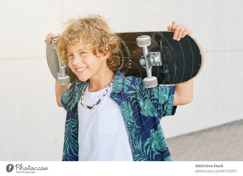Porträt eines Jungen, der ein Skateboard auf dem Rücken trägt und lächelt Jugendzeit Vitalität Selbstständigkeit tragen Teenager modisch posierend Gleichgewicht