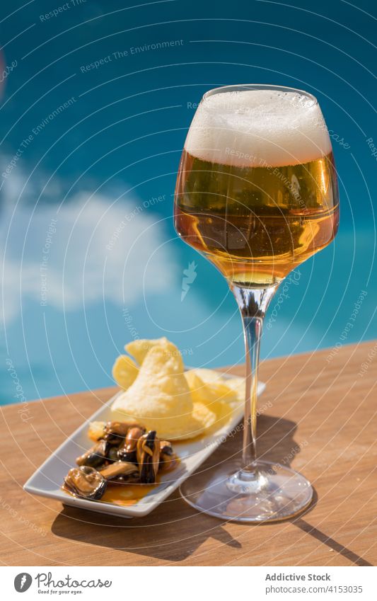 Ein Glas Bier und Snacks am Pool trinken frisch Getränk Alkohol Erfrischung cool geschmackvoll Miesmuschel Zitrone kalt lecker Feinschmecker dienen Beckenrand