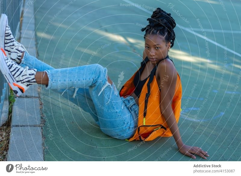 Fancy ethnischen Frau in stilvollem Outfit sitzen auf dem Boden in der Straße Mode Stil trendy urban Afroamerikaner Hipster jung ausgefallen schwarz