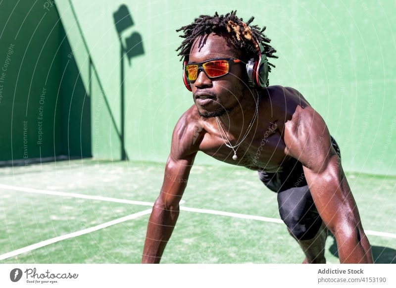 Starker männlicher Sportler, der auf dem Sportplatz Musik hört zuhören Training Mann Aufwärmen Dehnung Bestimmen Sie nackter Torso Kopfhörer ethnisch schwarz