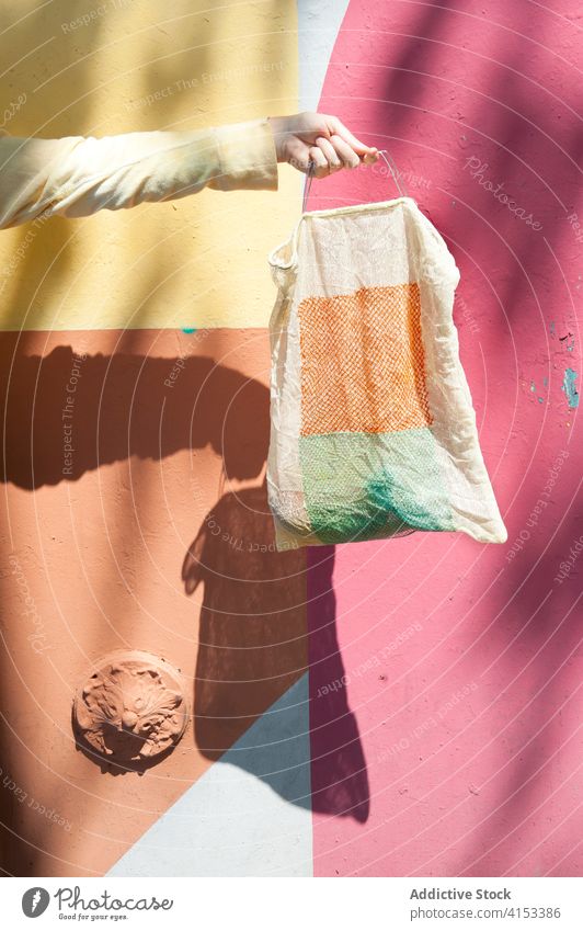 Crop-Frau mit bunter Einkaufstasche umweltfreundlich Textil Gewebe Großstadt Straße Farbe Sonnenlicht lebhaft pulsierend Ökologie Wand Stil urban trendy Mode