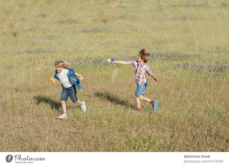 Inhalt Geschwister spielen zusammen auf einem Feld Wasser Pistole Kind Zusammensein Bruder Geschwisterkind Spaß haben Sommer Wiese positiv Freude heiter Gras