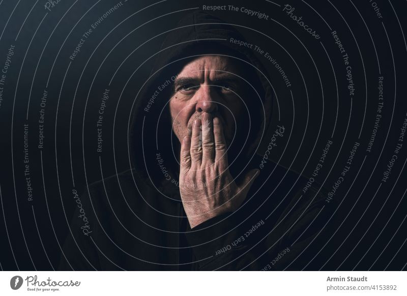 Porträt eines Mannes mit Kapuzenpulli, der sich eine Hand vor den Mund hält Winkel verboten Vollbart schwarz Unschärfe Atem lässig Kaukasier Nahaufnahme