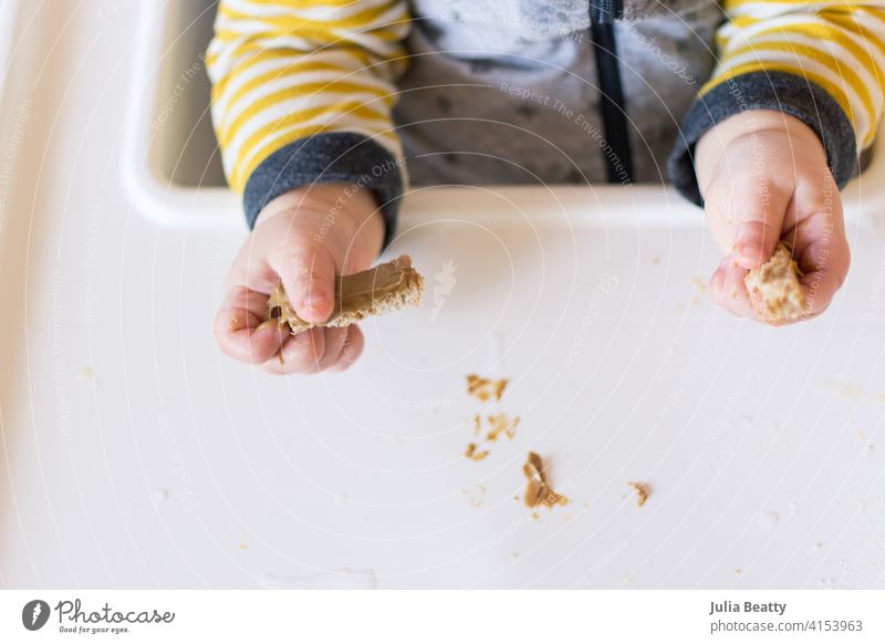 Kleinkinderhände halten Brotstreifen mit Erdnussbutter darauf; frühe Exposition gegenüber allergenen Lebensmitteln durch babygeführte Entwöhnung 6-12 Monate alt