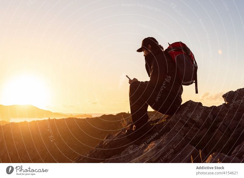 Männlicher Reisender, der in den Bergen auf seinem Smartphone surft Wanderer Mann Sonnenuntergang Berge u. Gebirge Browsen zuschauend bewundern benutzend