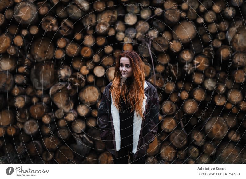 Frau in warmer Kleidung steht in der Nähe von gestapelten Holzstämmen Totholz Stapel hölzern Herbst Saison Holzstapel Jacke warme Kleidung reisen jung