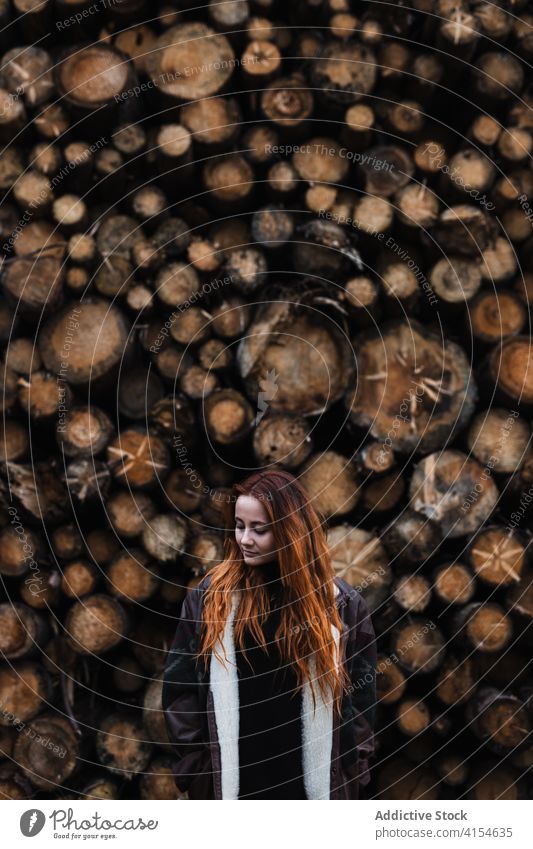 Frau in warmer Kleidung steht in der Nähe von gestapelten Holzstämmen Totholz Stapel hölzern Herbst Saison Holzstapel Jacke warme Kleidung reisen jung