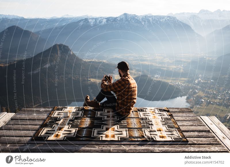 Reisender Mann sitzt auf einem Hügel und bewundert die Aussicht auf die Berge Fotograf Fotoapparat Aussichtspunkt Berge u. Gebirge unter Tourist Landschaft Kamm