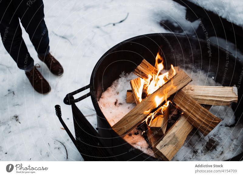 Anonyme Person, die im Winter in der Nähe eines Lagerfeuers steht Freudenfeuer Brennholz Flamme Aufwärmen Reisender Schnee Feuer Feuerstelle kalt Saison
