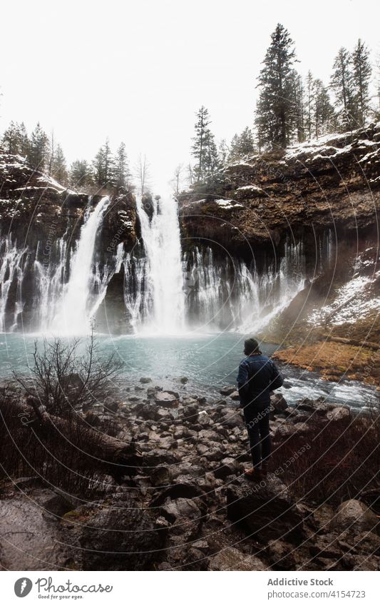 Anonyme Person an einem Wasserfall in einem verschneiten Bergwald an einem Wintertag Wald Schnee fließen Natur Landschaft Pool kalt strömen malerisch reisen