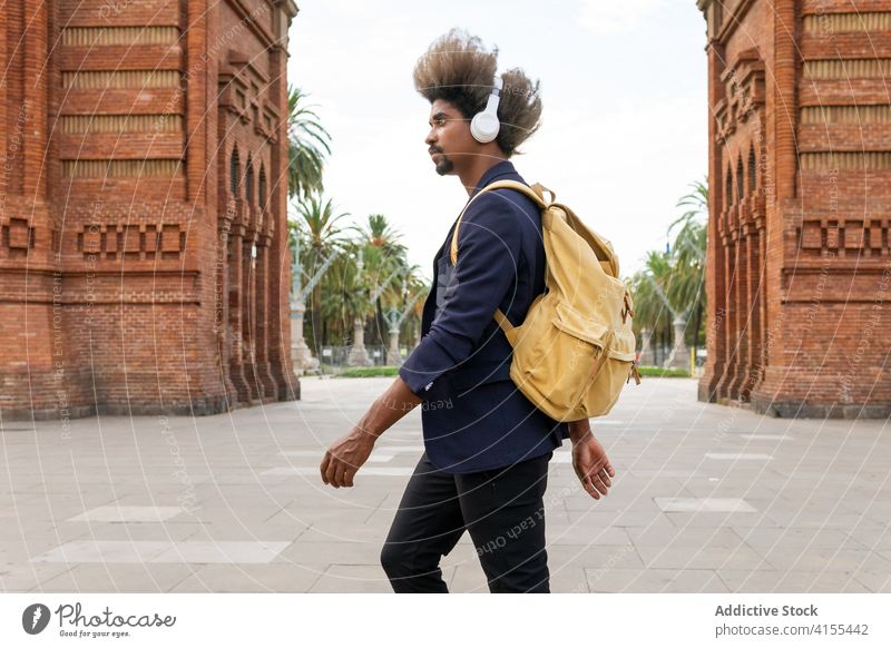Schwarzer Mann mit Afro-Haar und Freizeitanzug geht die Straße entlang Melodie entspannt hören lebhaft ethnisch Klang Apparatur genießend positiv trendy