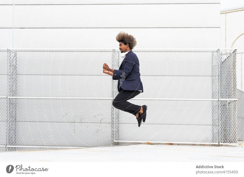Stilvoller schwarzer Mann springt in der Nähe eines Gebäudes in der Stadt Geschäftsmann springen Moment Großstadt Unternehmer Manager sorgenfrei Freiheit