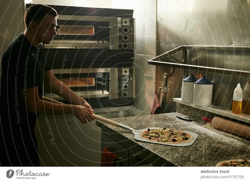 Mann nimmt rohe Pizza vor dem Backen auf die Schaufel nehmen schaufeln Koch vorbereiten Ofen Tradition Italienisch Küche Bestandteil Lebensmittel Prozess