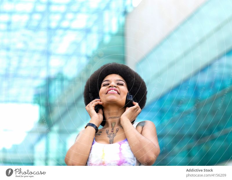 Fröhliche ethnische Frau beim Musikhören in der Stadt genießen Kopfhörer zuhören sorgenfrei Straße Sommer Drahtlos Freiheit schwarz Afroamerikaner Freude Gerät