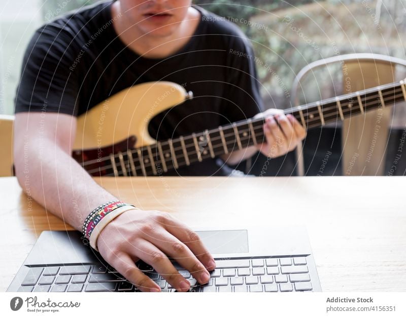 Mann mit Gitarre und Laptop Bass Musik benutzend lernen spielen zuschauen Instrument Tutorial Fähigkeit Musiker Melodie Gesang Hobby jung männlich Apparatur