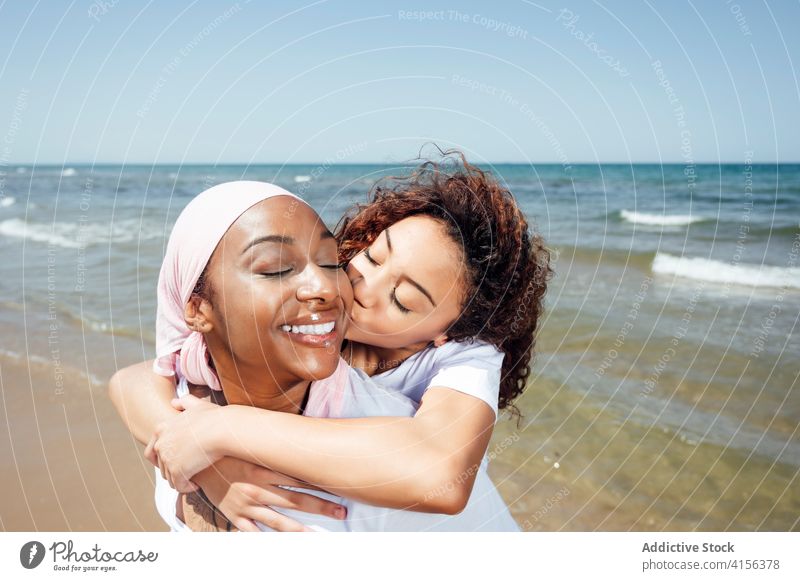 Fröhliche Mutter nimmt ihre Tochter am Strand huckepack Huckepack Mitfahrgelegenheit Spaß haben Bonden Partnerschaft heiter Zusammensein ethnisch schwarz