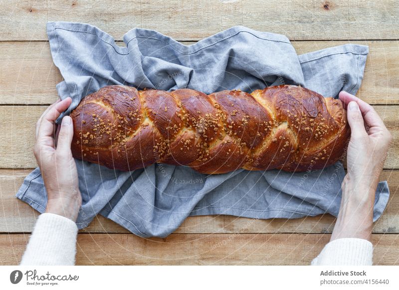 Person hält einen Laib frisches, geflochtenes Brot auf dem Tisch Geflecht Brotlaib gebacken Samen ganz Lebensmittel handgefertigt rustikal Gastronomie