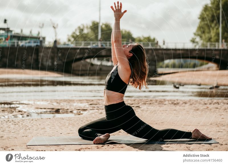 Frau in halber Taubenhaltung übt Yoga am Strand Halbe-Taube-Pose beweglich Asana ardha kapotasana üben Achtsamkeit Stressabbau Sommer Unterlage sitzen BH