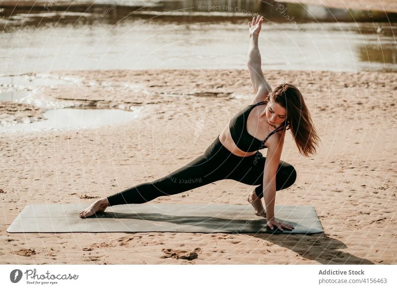 Friedliche Frau macht Yoga in Skandasana am Flussufer Seitenlonge skandasana Pose ausdehnen Windstille Zen Körperhaltung Strand Unterlage Asana Gleichgewicht
