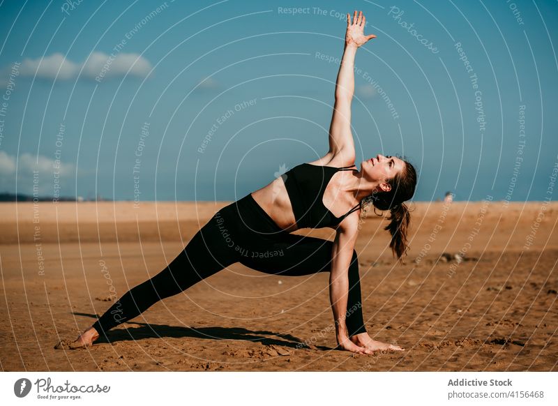 Flexible Frau beim Yoga in erweiterter Seitenwinkelhaltung erweiterte Seitenwinkelstellung Strand Pose üben beweglich Sommer Asana schlank Sportbekleidung