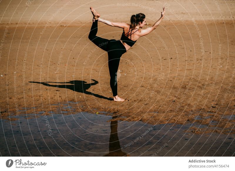 Anonyme Frau beim Yoga in "Lord of the Dance"-Pose Herr der Tanzpose Natarajasana Gleichgewicht Strand üben beweglich Asana Fluss Ufer passen Windstille Natur