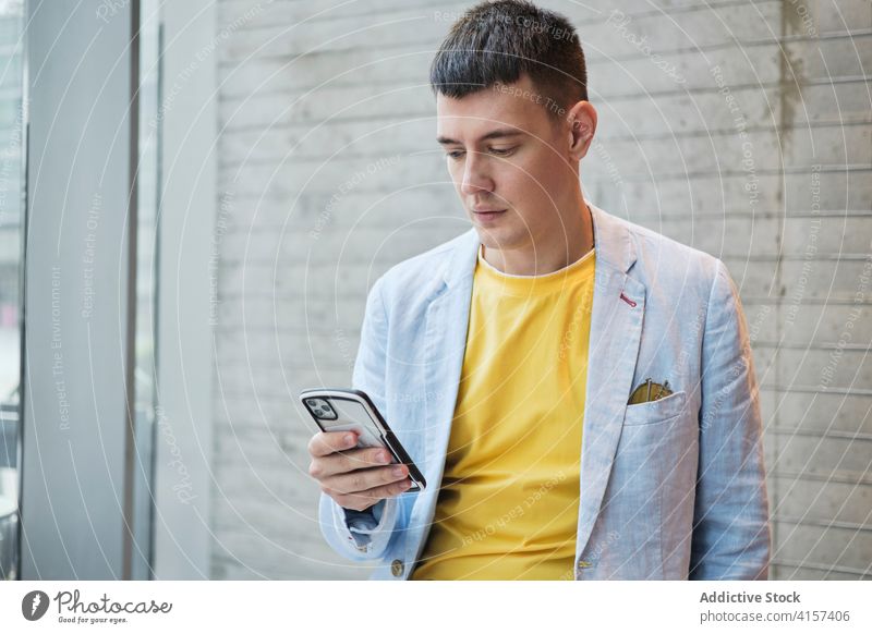 Mann in trendigem Outfit benutzt Smartphone im Büro Geschäftsmann Stil hell Arbeitsplatz benutzend ernst trendy Arbeitsbereich Browsen männlich Unternehmer