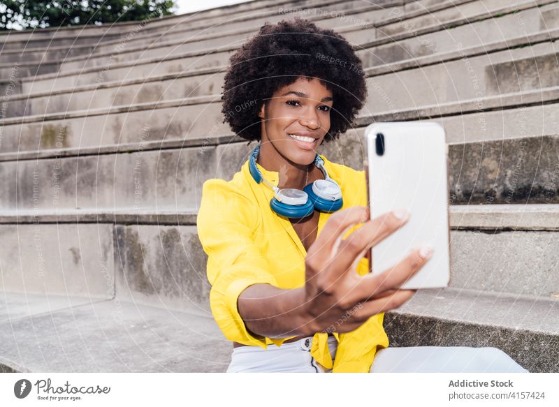 Fröhliche schwarze Frau macht Selfie in der Stadt Selbstportrait Afro-Look Frisur Großstadt Smartphone benutzend charmant Lächeln ethnisch Afroamerikaner heiter