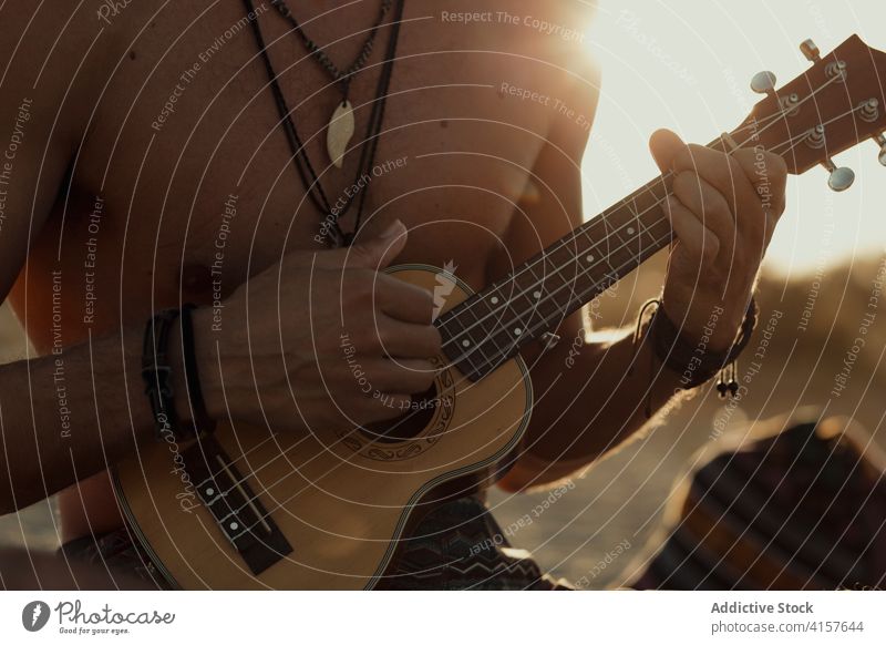 Kreativer Mann spielt Ukulele am Strand spielen Hippie unterhalten akustisch Musik kreativ männlich Sonnenuntergang Sommer Ufer ruhen Urlaub Wochenende Gitarre