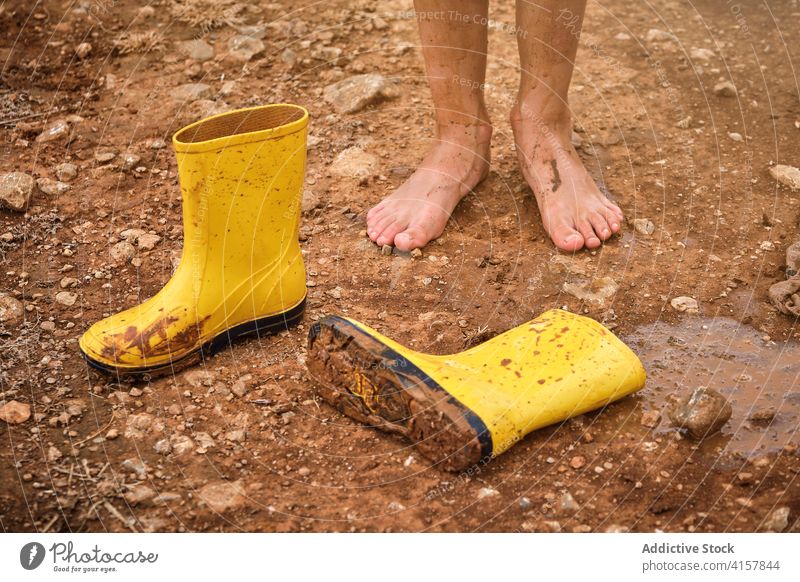 Schmutzige, schlammige nackte Füße mit einem Paar Wasserstiefel auf einem schlammigen Weg Schuljunge Lebensstile unordentlich Wochenende Problematik Fuß Regen