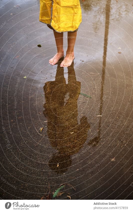 Vertikales Foto einer barfuß gehenden Person in einem Regenmantel, die sich in einer Pfütze spiegelt schlecht dramatisch Haut nass Wetter Tropfen