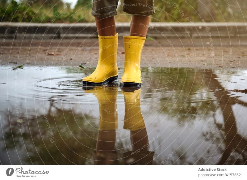 Beine eines Jungen mit gelben Regenstiefeln in einer Wasserpfütze auf einem Weg Lebensstile unordentlich stehen Kinder nass Wetter Freude spielen Tropfen