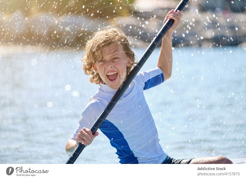 Porträt eines Jungen auf einem Paddel-Surfbrett, der mit dem Paddel spielt Vitalität gestikulieren platschen Lachen sitzen anheben anhaben Gleichgewicht