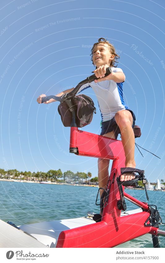 Junge fährt auf einem Wasserfahrrad mit Glücksausdruck Lebensstile Mitfahrgelegenheit Wellness gestikulieren Herausforderung Gleichgewicht Befriedigung Männer