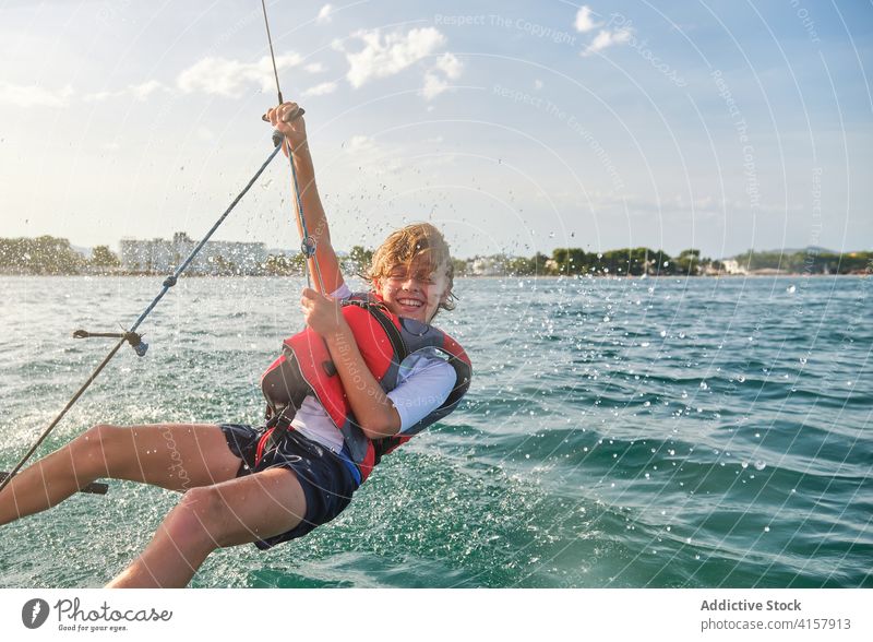 Wassertropfen bespritzen ein Kind, das sich ein Seil von einem Boot schnappt, um Gegengewichte zu machen, die auf das Meer hinaushängen Lachen Verantwortung