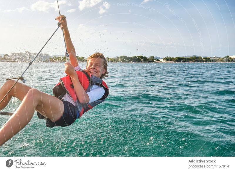 Wassertropfen bespritzen ein Kind mit einer Schwimmweste, das an einem Seil eines Bootes auf dem Meer hängt Freiheit Gegengewicht Lachen gestikulieren Gewicht