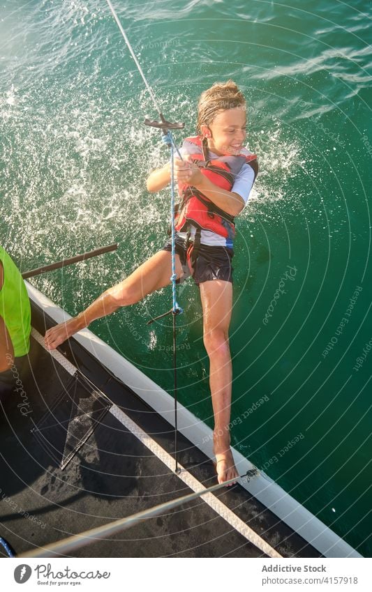 Junge mit Schwimmweste an einem Seil hängend beim Segeln im Meer mit einem Boot Rennen Unterstützung gestikulieren Gewicht platschen Weg Wind Verantwortung