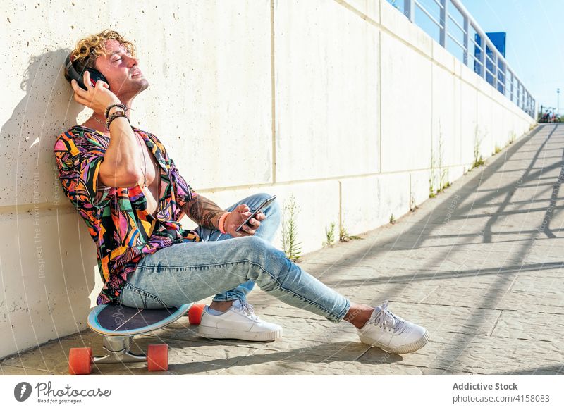 Entspannter männlicher Skater beim Musikhören in der Stadt zuhören Mann sich[Akk] entspannen genießen urban trendy Hipster Kopfhörer Skateboard Straße verträumt