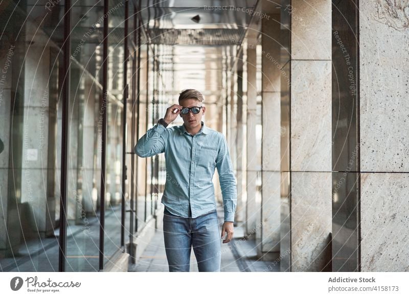 Stilvoller Mann mit Sonnenbrille in der Stadt smart lässig Großstadt trendy selbstbewusst emotionslos gutaussehend Gebäude männlich modern Outfit ernst urban