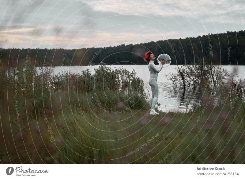 Frau im Astronautenanzug steht in der Nähe von Wasser futuristisch Raum Schutzhelm Anzug Fluss Natur Kosmonaut Konzept Silber Zukunft Phantasie Wissenschaft