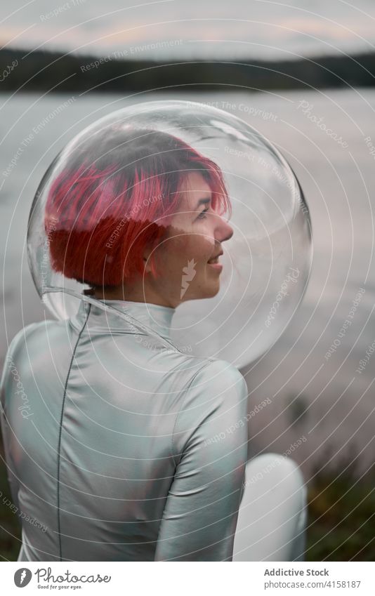 Frau im Astronautenanzug sitzt am Wasser futuristisch Raum Schutzhelm Anzug sitzen Fluss Natur Lächeln Kosmonaut Konzept Silber Zukunft Phantasie Wissenschaft